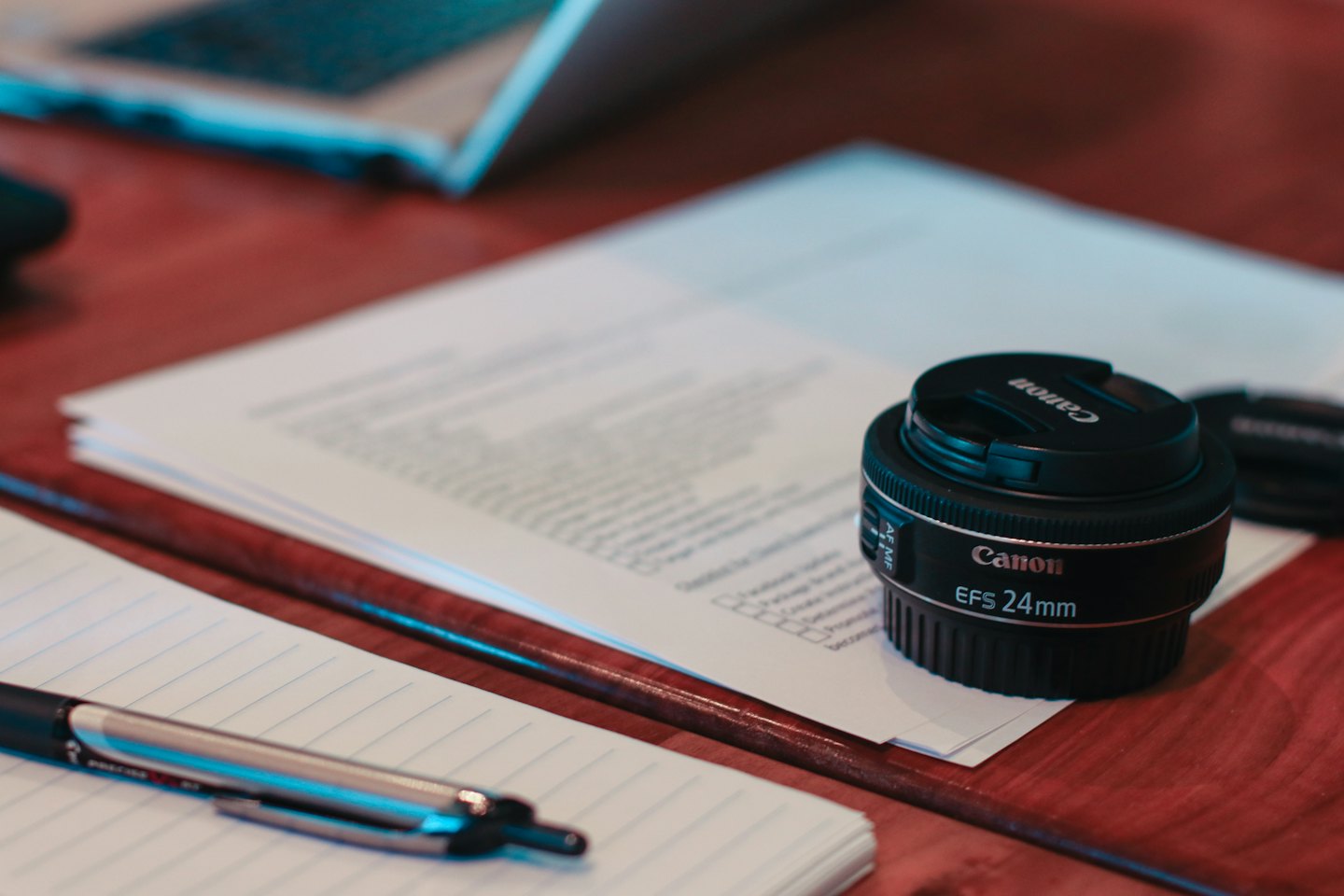 Black camera lens on white papers on a wooden desk.
